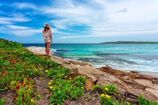 Female dressed in casual beach clothes stands on rocks admiring the beautiful beach and coast in Australia.Location: Maroubra Beach