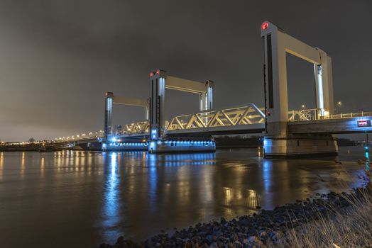 ROTTERDAM, 21 March 2019 - View of the Botlek bridge at the entrance of Rotterdam city by boats reflection on the calm water against a chemical industrial compound lighting the night sky, Netherlands