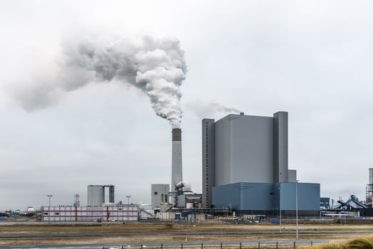 Rotterdam power station splitting chem-tray in the sky through its hight chimney in the industrial area in the Maasvlakte, Netherlands