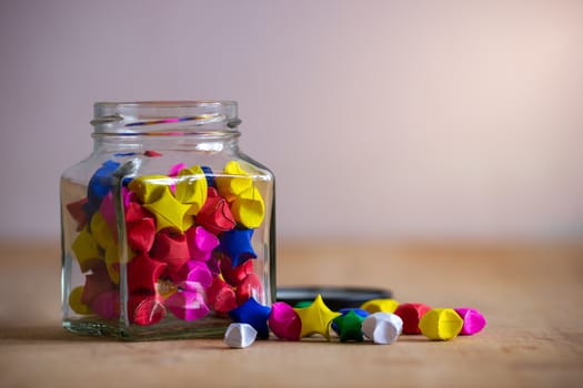 Multicolor paper star in square glass bottle on wooden table with morning sunlight.