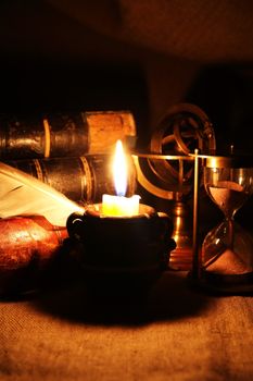 Vintage still life with hourglass near lighting candle and books