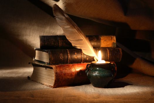 Vintage still life with quill pen near lighting candle and books