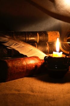 Vintage still life with quill pen near lighting candle and books
