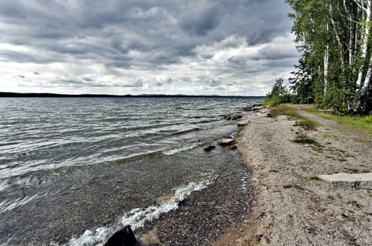 view of the lake with cumulonimbus clouds above it in windy weather