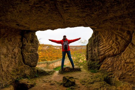 woman looks from the mountain to a beautiful autumn forest, arms outstretched