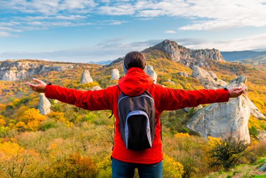 A tourist with a backpack with open arms enjoying the autumn landscape in the mountains