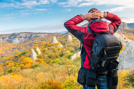 Photographer traveler with a backpack admiring beautiful mountains in autumn, rear view
