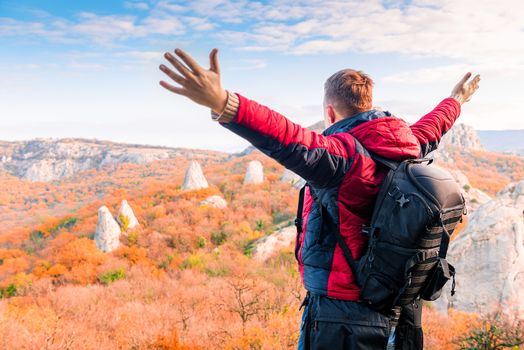tourist with a backpack with open arms enjoying the autumn landscape in the mountains