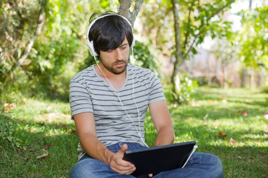 young man relaxing with a tablet pc listening music with headphones on a the park, outdoor