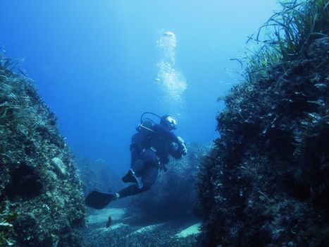 a diver passes between large stones covered with algae, the bubbles of his breathing rise to the surface of the crystalline blue and turquoise water illuminated by the sun