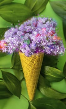 Waffle cone with violet flowers with leaves on green background