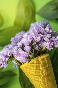 Waffle cone with violet flowers with leaves on green background