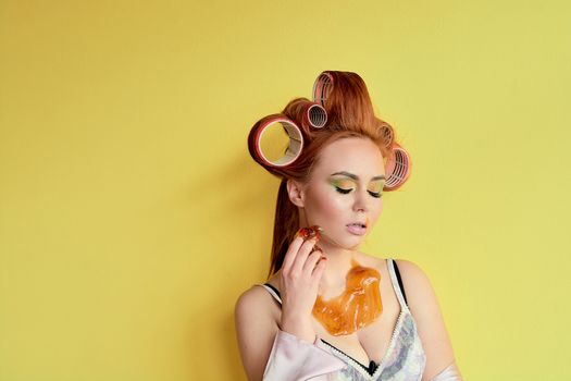 Young redhead woman with shugaring paste on her hands, face, body and chest. Young redhead woman with hair curlers. Advertising concept of shugaring paste. Skin care concept with copyspace.