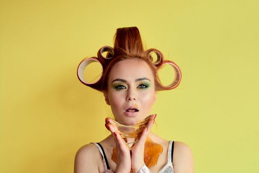 Young redhead woman with shugaring paste on her hands, face, body and chest. Young redhead woman with hair curlers. Advertising concept of shugaring paste. Skin care concept with copyspace.