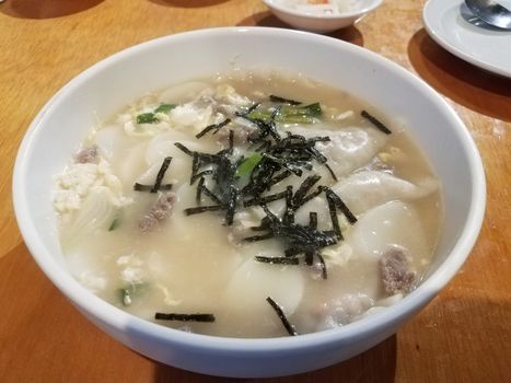 Korean soup with dumplings and seaweed in bowl on table