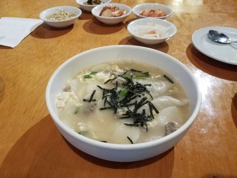 Korean soup with dumplings and seaweed in bowl on table