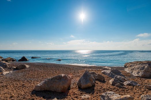 Sandy beach, large stones, blue sea and bright sun - beautiful seascape