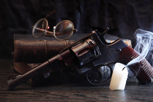 Still life with old revolver near book and extinguished candle