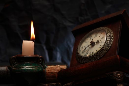 Vintage still life with lighting candle near old clock