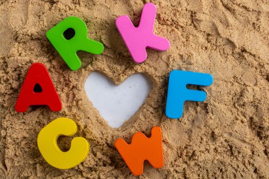 Heart shape and colorful Letters made of wood on sand