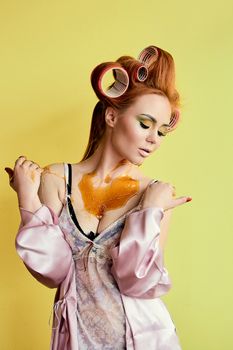 Young redhead woman with shugaring paste on her hands, face, body and chest. Young redhead woman with hair curlers. Advertising concept of shugaring paste. Skin care concept with copyspace.