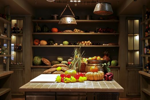 The interior design in rustic style, on a large table and on the shelves in cabinets are fresh vegetables and fruits.