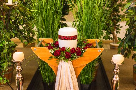 Funeral and mourning concept, crematorium white red urn on table in church