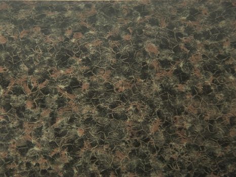 Natural stone granite of black-brown color with dark maroon impregnations. Close-up.