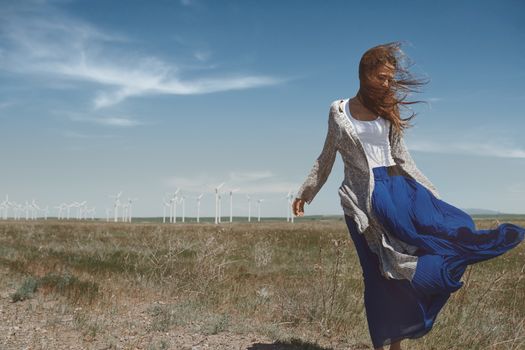 Woman with long tousled hair next to the wind turbine with the wind blowing