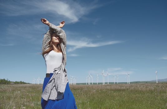 Woman with long tousled hair next to the wind turbine with the wind blowing