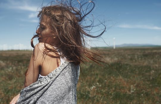 Woman with long tousled hair next to the wind turbine with the wind blowing