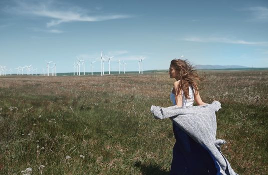 Woman with long tousled hair next to the wind turbine with the wind blowing