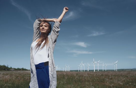 Woman with long tousled hair next to the wind turbine with the wind blowing