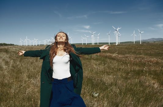 Woman with long tousled hair next to the wind turbine with the wind blowing