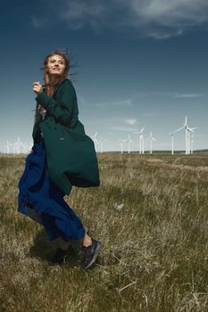 Woman with long tousled hair next to the wind turbine with the wind blowing