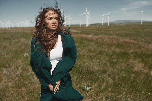 Woman with long tousled hair next to the wind turbine with the wind blowing