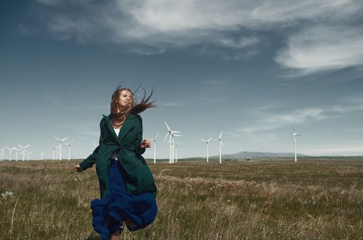 Woman with long tousled hair next to the wind turbine with the wind blowing