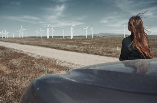 Woman leaning to her car next to the wind turbines site