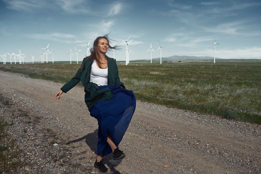 Woman with long tousled hair next to the wind turbine with the wind blowing