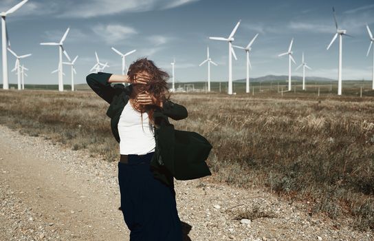 Woman with long tousled hair next to the wind turbine with the wind blowing