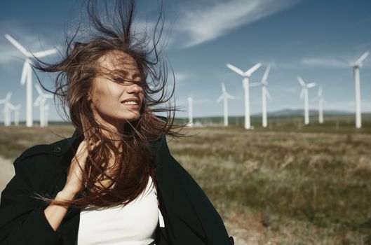 Woman with long tousled hair next to the wind turbine with the wind blowing