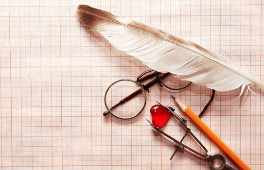 Old spectacles and measuring tools around red glass heart on graph paper