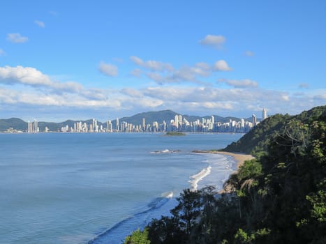 View of the coast, with city in the background and forest in the foreground, at dusk with shadows