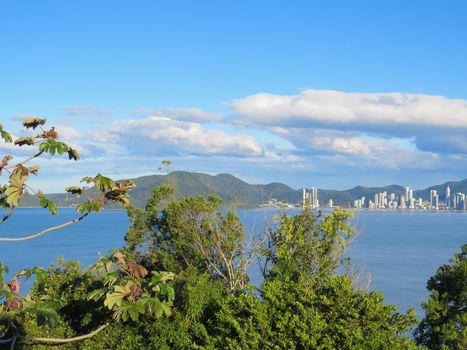 Coastal city landscape with forest in the foreground, late afternoon in blue sea