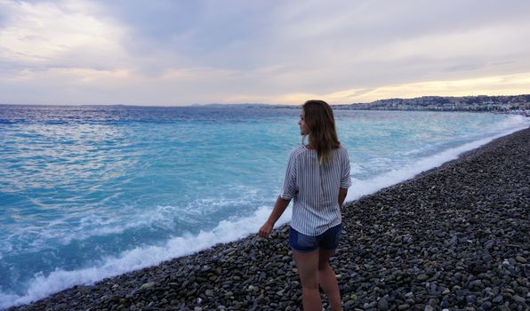 NICE, FRANCE. Young woman enjoying the azure coast and looking at the sea. Beach of pebbles.