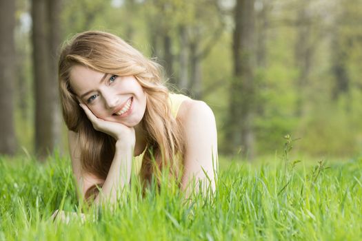 Blonde pretty girl laying on the grass in spring park and smiling