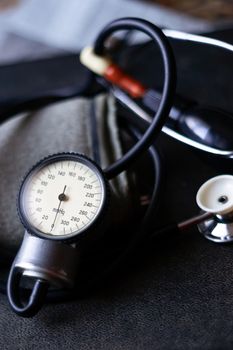 Analog tonometer with cuff and phonendoscope on old suitcase. Close up view and blurred background. Underexposed photo.