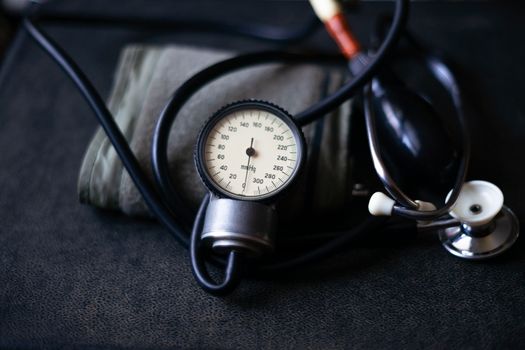 Analog tonometer with cuff and phonendoscope on old suitcase. Close up view and blurred background. Underexposed photo.