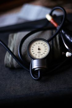 Analog tonometer with cuff and phonendoscope on old suitcase. Close up view and blurred background. Underexposed photo.