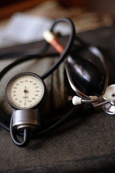 Analog tonometer with cuff and phonendoscope on old suitcase. Close up view and blurred background. Underexposed photo.